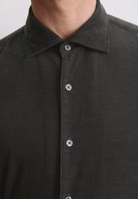 Chemise en velours côtelé gris foncé avec un col classique, comportant six boutons métalliques et une surface de tissu texturée.