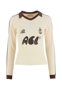 Pitkähihainen kermavärinen poolopaita, jossa on ruskea kaulus ja hihansuut. Paidassa on musta graafinen logo ja pyöristetty helma. Se on valmistettu pehmeästä, teksturoidusta kankaasta.