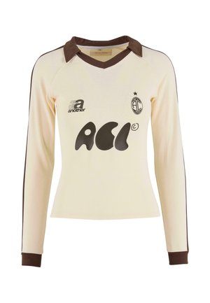 Jersey crème à manches longues avec col et poignets marron, présentant un logo graphique noir et un ourlet arrondi. Fabriqué à partir d'un tissu doux et texturé.