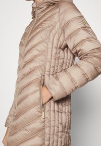 Champagnefarvet dunjakke med chevron-syning, lynlåslommer og høj krave. Har teksturerede sidelommer og guldfarvet hardware.