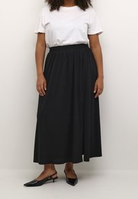 Zwarte maxi rok met een elastische tailleband, gecombineerd met een wit t-shirt. De rok heeft een soepele textuur en een volle, vloeiende uitstraling.