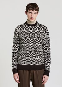 Knit sweater featuring a geometric pattern in black and white, crew neck, and ribbed cuffs and hem, paired with brown trousers.