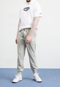 Vitt bomullströja med svart grafiskt tryck, kombinerad med ljusgrå sweatpants. Vita sneakers med svarta detaljer fulländar outfiten.