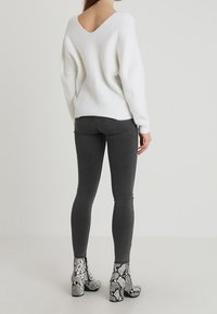 Weißer gerippter Pullover mit einem weiten V-Ausschnitt, kombiniert mit dunkelgrauen Slim-Fit-Jeans und gemusterten grauen Ankle-Boots im Schlangenlederlook.
