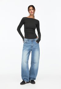 Schwarz langärmliges Oberteil mit enger Silhouette, kombiniert mit hellblauen, sackartigen Jeans mit einzigartigen Vorderstich-Details und lockerer Passform.
