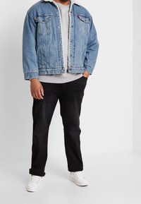 Jeansjacka i ljusblått med krage i vitt päls, grå sweatshirt under, svarta byxor och vita sneakers. Enkel, avslappnad outfit.