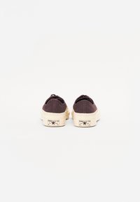 Hnědé plátěné tenisky s krémovými gumovými podrážkami a akcenty loga, s zaoblenými patami a minimalistickým designem.