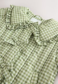 Grüne gesteppte Vichyjacke mit gerafftem Kragen und Schleifendetails. Hergestellt aus leichtem Stoff mit kariertem Muster.