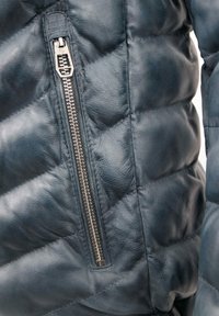 Dunkelblaue Lederjacke mit gestepptem Muster, ausgestattet mit einer silbernen Reißverschlusstasche und glattem Stoff.