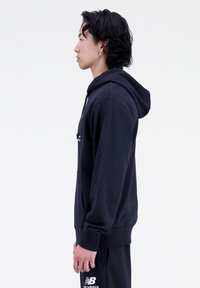 Sudadera azul marino de tejido suave con capucha ajustable. Cuenta con un bolsillo tipo canguro y puños acanalados, mostrada en vista lateral.
