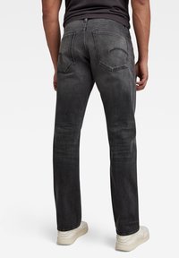 Jeans de denim gris oscuro con un diseño de pierna recta, que cuentan con dos bolsillos traseros y un desgaste mínimo. Combinados con zapatillas blancas.