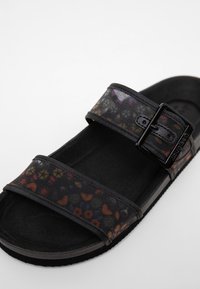Sandale noire à bout ouvert avec deux larges brides, dont une avec une boucle noire et un motif floral multicolore subtil.