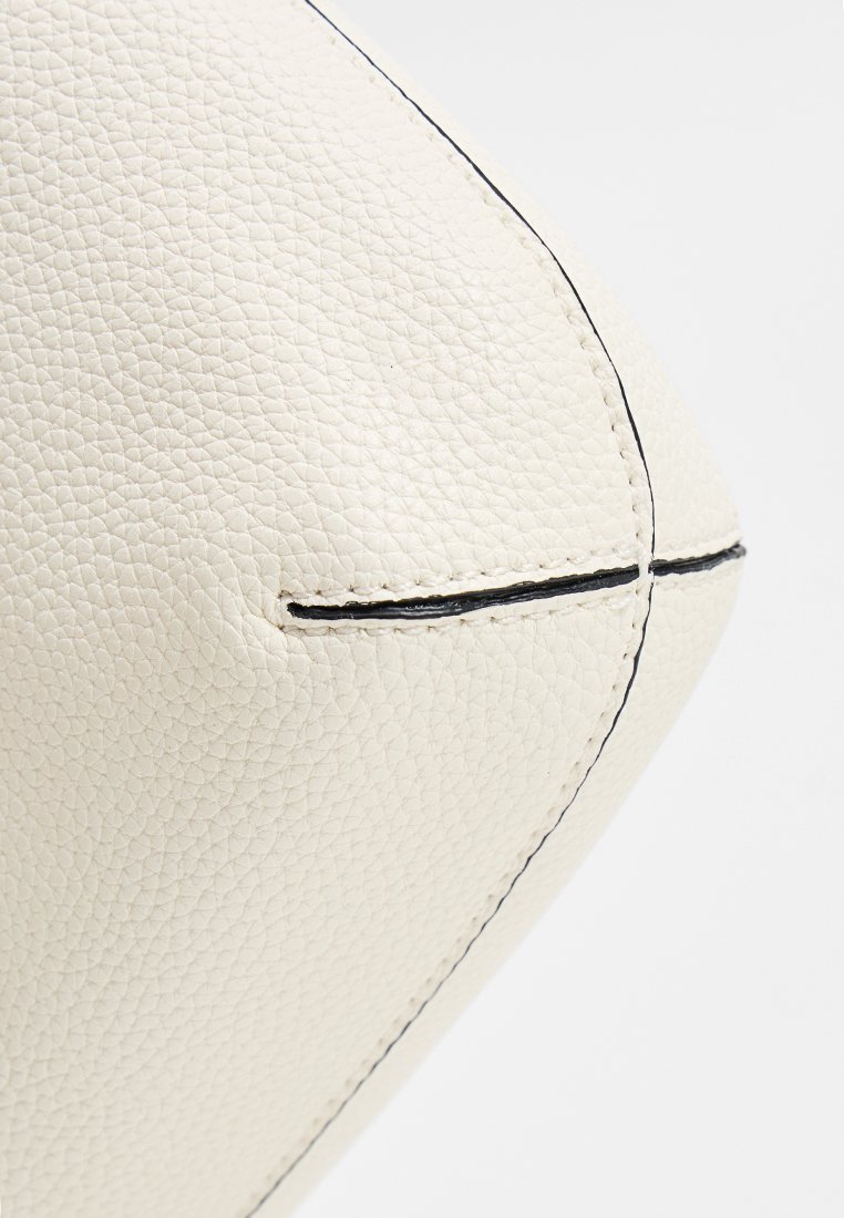Cuir blanc texturé avec une finition granuleuse, présentant des coutures noires contrastantes le long des coutures et des bords pour plus de détails.