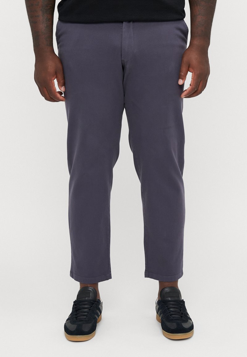 Marineblaue Freizeit-Hosen mit schlanker Passform, leichtem Stoff und glatter Textur. Getragen mit schwarzen Trainingsschuhen mit Gummisohlen.