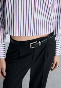 Pantaloni negri croiți, cu o curea lucioasă din piele neagră. Cămașa este albă, cu dungi verticale roșii și albastre, tăiată la talie.