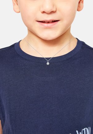 Zilveren ketting met een kleine glimlachende hangers, gedragen door een kind in een marineblauw shirt. De ketting lijkt delicaat en eenvoudig te zijn.