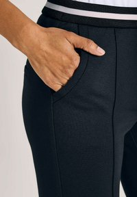 Hand rustend in de voorzak van zwarte broek met een gestreepte tailleband.
