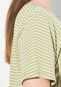 Top de manga corta color oliva con rayas blancas horizontales. Tejido suave con un corte holgado, presenta un escote redondeado y dobladillos cosidos.