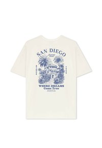 Camiseta de algodón de color crema con un diseño gráfico azul de palmeras y un edificio con el texto "SAN DIEGO" y "DONDE LOS SUEÑOS Se Hacen Realidad."