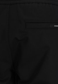 Svarta byxor i slätt tyg, med en bakficka och en liten etikett med ordet "CHASING" i vitt. Enkel, funktionell design.