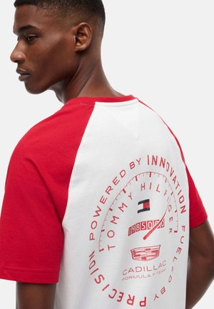 Uomo che indossa una maglietta raglan bianca e rossa con un logo circolare Tommy Hilfiger e Cadillac sulla schiena.