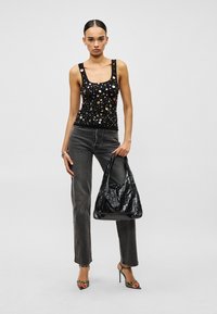 Schwarzes Tanktop mit mehrfarbigen runden Verzierungen, kombiniert mit hoch taillierten grauen Jeans und einer glänzenden schwarzen Schultertasche.