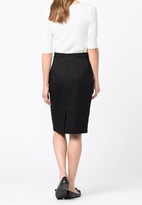 Černá tužková sukně se zadním rozparkem, strukturovaný design, vyrobená z hladkého materiálu. V kombinaci s bílým topem, pohled zezadu.