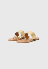 Goldene Rutschsandalen mit geflochtenen Riemen, flacher Sohle und einem dekorativen metallischen Akzent an der Zehe. Glatte, beige Innensohle und leichtes Design.