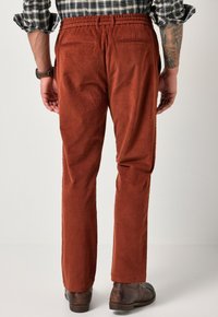 Nauhka-housut syvän oranssina, joissa on joustava vyötärö, kaksi takataskua, suora leikkaus ja pehmeä pinta.