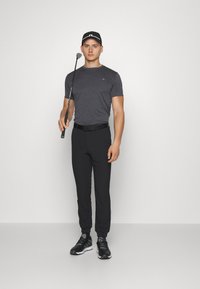 Gray short-sleeve shirt, black pants, black cap, holding a golf club. The outfit features a sporty design suitable for golfing.