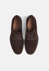 Bruine suède schoenen met een ronde neus, voorzien van een vetersluiting en subtiele stikdetails. Gladde leren binnenzool gemarkeerd met "VAGABOND."
