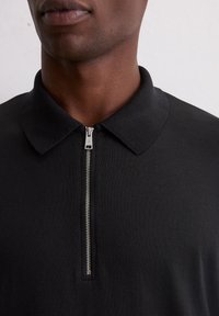 Zwart poloshirt met een kraag met ritssluiting; gestructureerde stof en een slank, aansluitend silhouet; zilveren ritssluitingdetail voegt een modern accent toe.