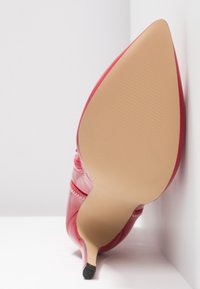 Escarpin à talon aiguille en cuir verni rouge avec bout pointu, présentant une surface lisse et une semelle extérieure beige texturée à motif côtelé.