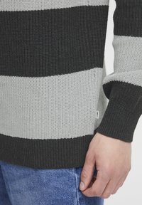Pulover tricotat cu dungi orizontale negre și gri deschis, țesătură texturată, manșete ribbate și o etichetă mică de marcă pe lateral.