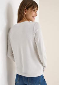 Maglione grigio chiaro realizzato in un materiale lavorato a maglia, con scollo rotondo e maniche lunghe, abbinato a jeans blu.