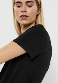 Schwarzes T-Shirt mit kurzen Ärmeln und rundem Ausschnitt, aus weichem Stoff und mit umgeschlagenen Ärmeln. Glatter Stoff mit taillierter Passform.