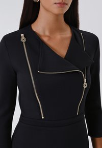 Schwarzes Wickelkleid mit tiefem V-Ausschnitt, dreiviertel Ärmeln und goldenen Reißverschlüssen mit dekorativen Akzenten auf den Schultern. Glatte Textur.