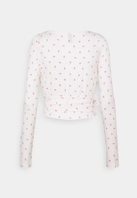 Dlouhý rukáv upnutý top z měkké bílé žebrované tkaniny s růžovým květinovým vzorem a zavinovacím designem s detaily na vázání v oblasti pasu.