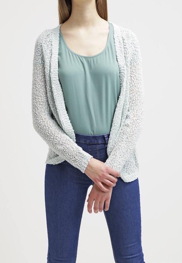 Licht mintgroene gebreide cardigan met een open voorkant, textuurstof en lange mouwen, gelaagd over een teal top en donkerblauwe jeans.