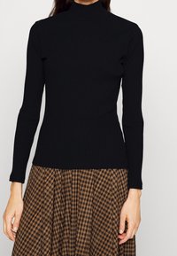 Zwarte geribbelde turtleneck trui met lange mouwen, gladde textuur, aansluitend ontwerp en een hoge hals. Gecombineerd met een geruite rok.