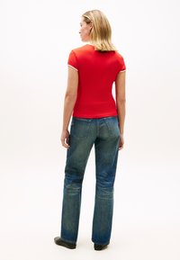 Κόκκινο κοντομάνικο μπλουζάκι με λευκή επένδυση, συνδυασμένο με μπλε τζιν παντελόνια φαρδιάς γραμμής. Ομαλό ύφασμα και casual σχεδιασμός, από πίσω.