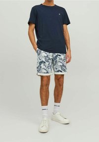 Camiseta de manga corta en color navy combinada con shorts blancos que presentan un patrón de hojas azules, completada con zapatillas blancas y calcetines que muestran un logo.