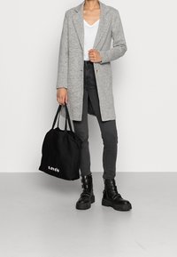 Grå lang blazer over en hvid V-hals skjorte, sorte skinny jeans og sorte platform støvler. Sort tote bag med "Levi's" logo.