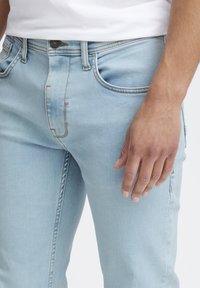 Ljusblå denimjeans med smal passform. Funktioner inkluderar fem fickor, subtil blekning och kontrasterande sömmar. Bomullstyg med slät textur.