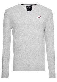 Sweater gris clair en V, fabriqué en matière tricotée douce, avec des manches longues et un ourlet côtelé. Présente un petit logo rouge sur la poitrine.