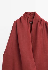 Veste en lin rouge rouille avec large col châle, drapé doux et étiquette de marque visible à l'intérieur du col.