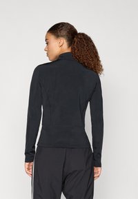 Čierny dlhý rukáv športový top s vysokým golierom, hladkou textúrou, priliehavým strihom a kontrastným prešívaním, skombinovaný s čiernymi športovými nohavicami.