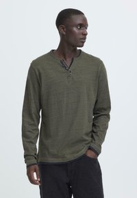 Hosszú ujjú khaki henley ing, texturált anyagból készült, három gombos gallérral és kontrasztos sötét mandzsettákkal.
