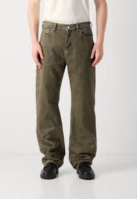 Cargo pants in olive green, made of textured fabric. Features a relaxed fit, multiple pockets, and tonal stitching. Paired with black shoes.