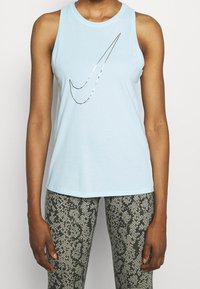 Vaaleansininen olkapäältä avattu toppi pehmeässä kankaassa, jossa on metallinhohtoinen Nike-logo. Yhdistetty tiukkoihin legginsseihin, joissa on käärmeennahkakuosi.